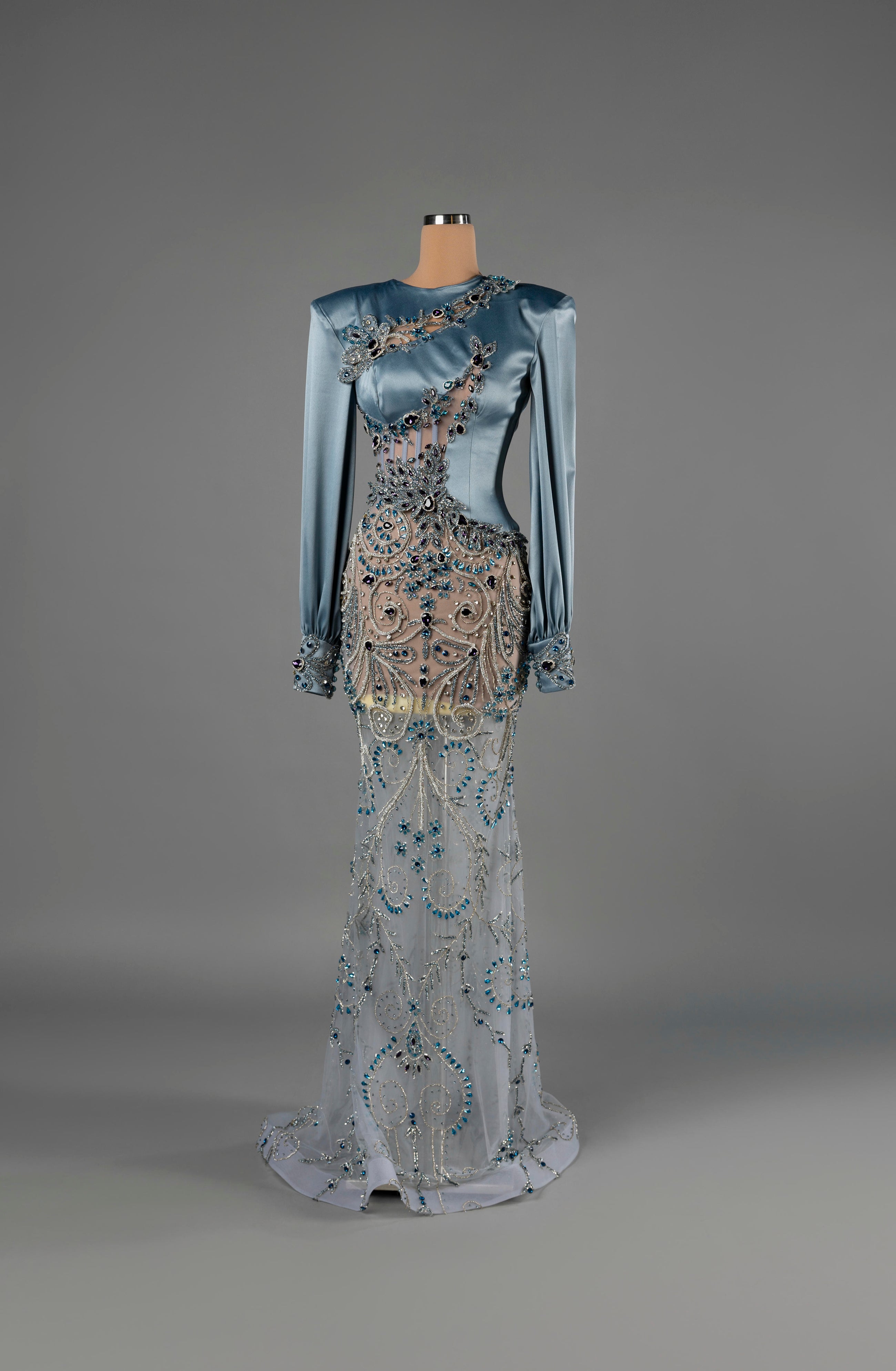 Sihëna Sapphire Enigma — powder-blue high-neck long-sleeve satin mermaid gown with sheer panels and blue crystal beadwork.
