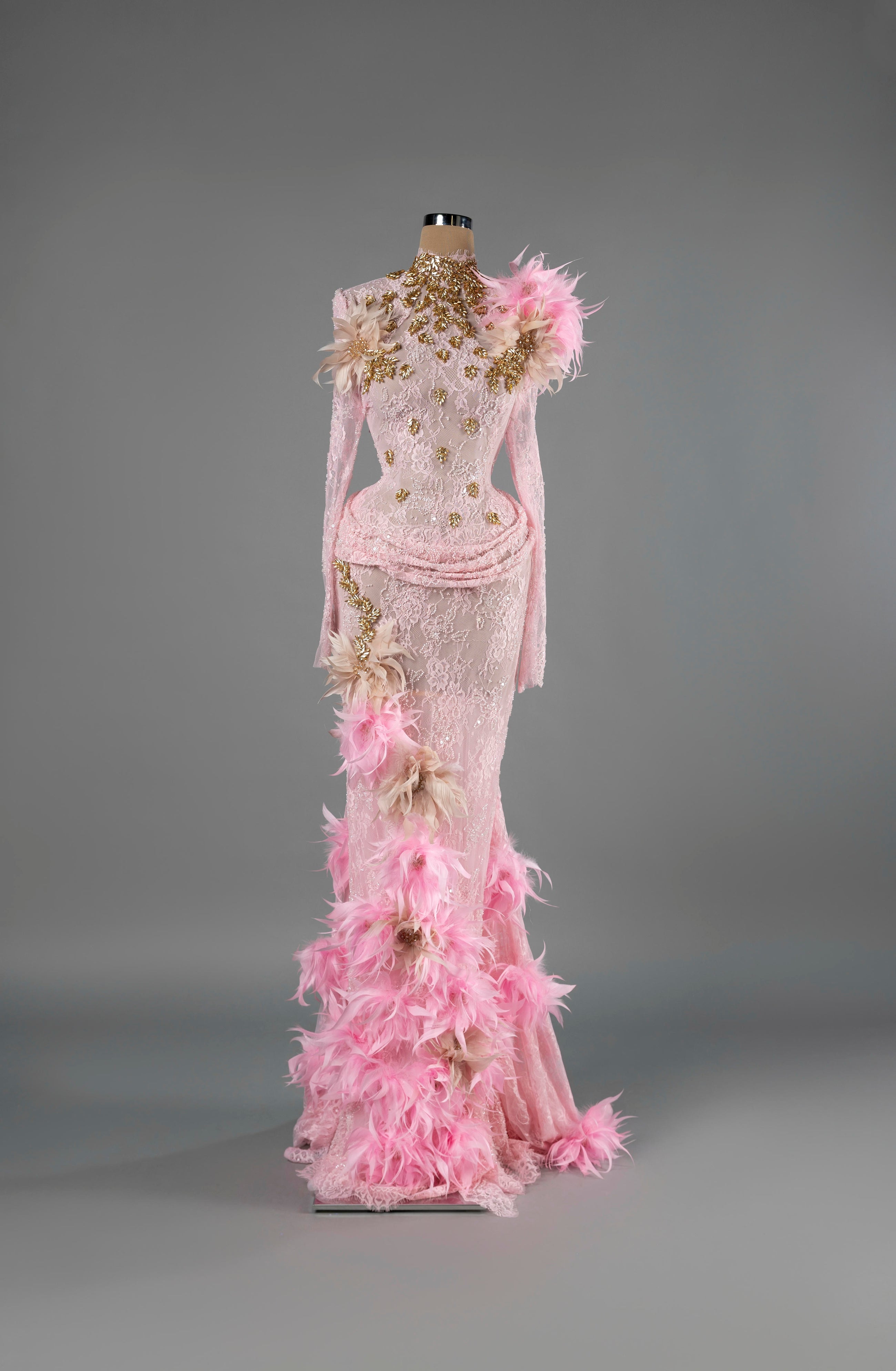 Sihëna Rose Plume — pink high-neck long-sleeve lace mermaid gown with gold leaf beadwork and pink feather floral trim.