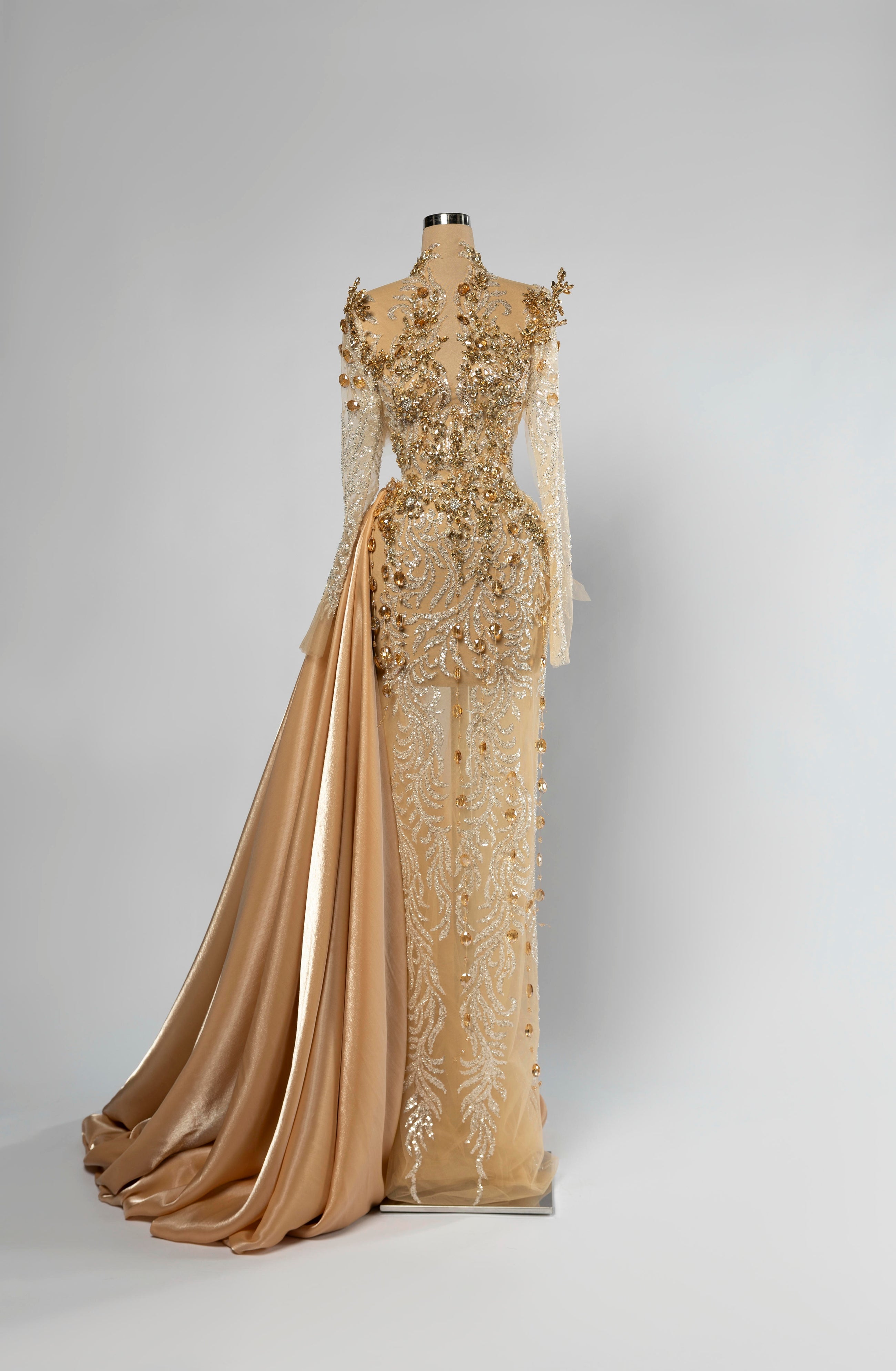 Sihëna Desert Marquise — champagne high-neck long-sleeve column evening gown in beaded tulle illusion with gold satin side overskirt.