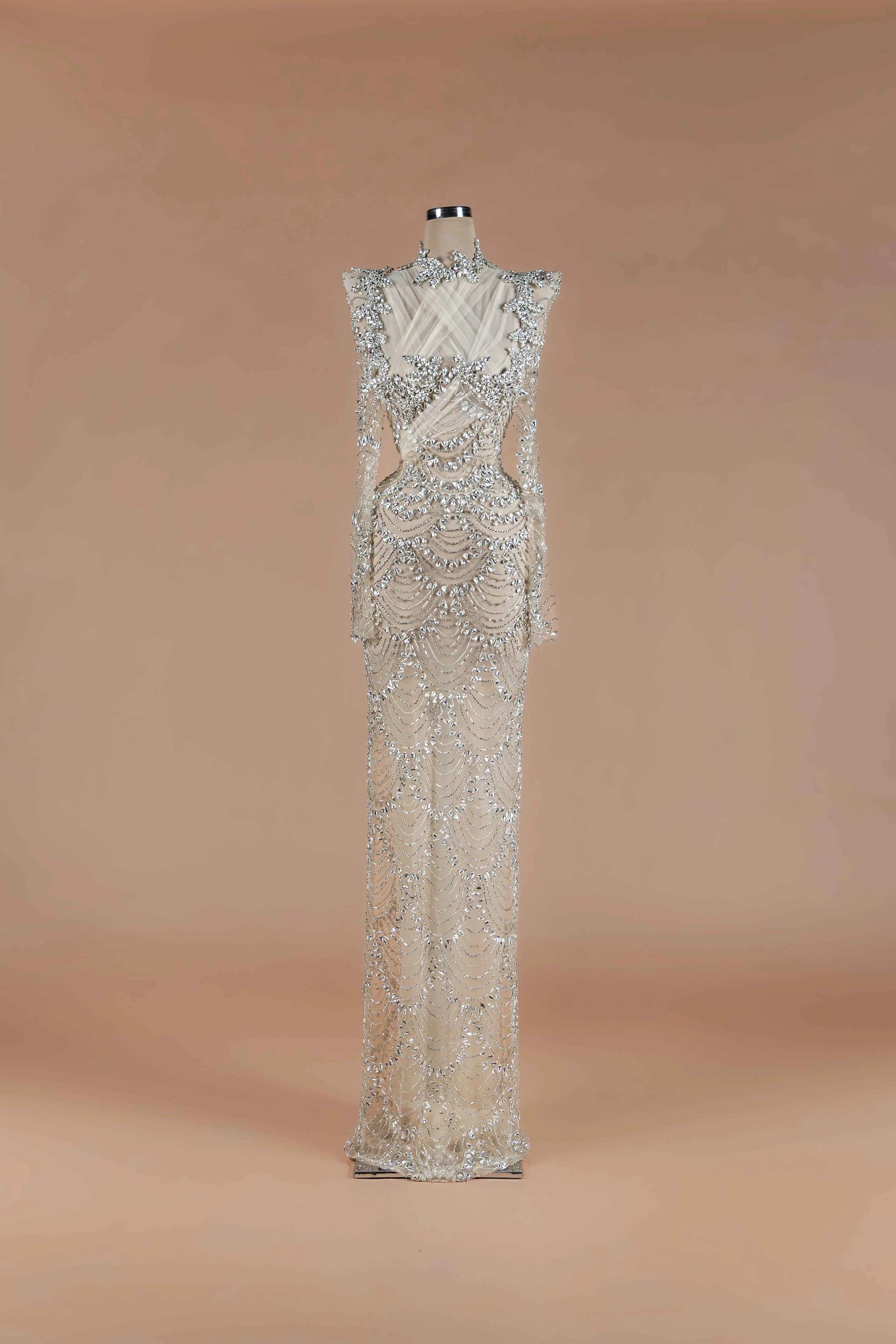 Sihëna Silver Scallop — silver high-neck long-sleeve column gown with scalloped crystal-pearl beadwork on sheer nude tulle.