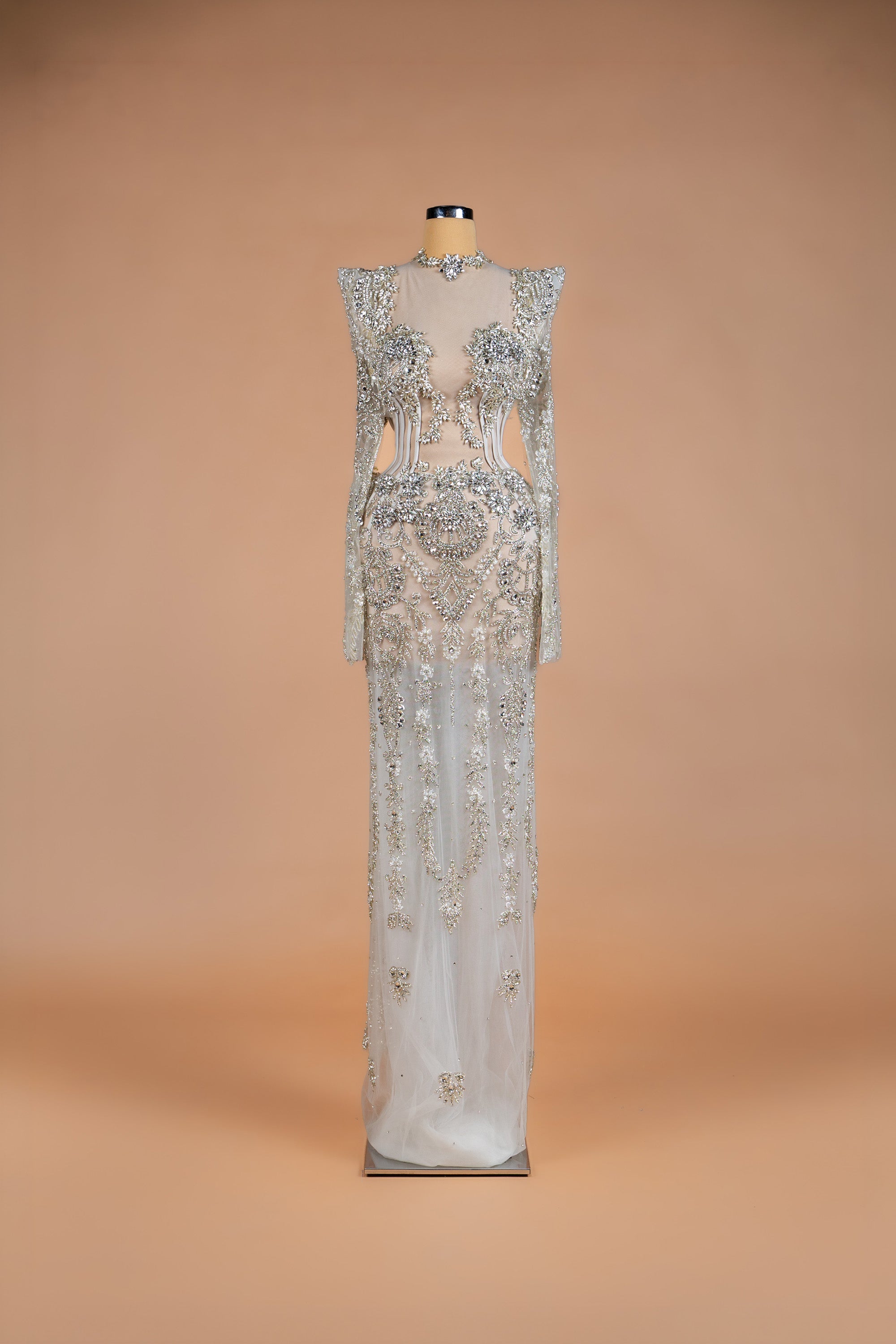 Sihëna Venetian Crystal — silver high-neck long-sleeve column gown with crystal floral beadwork on sheer nude illusion base.
