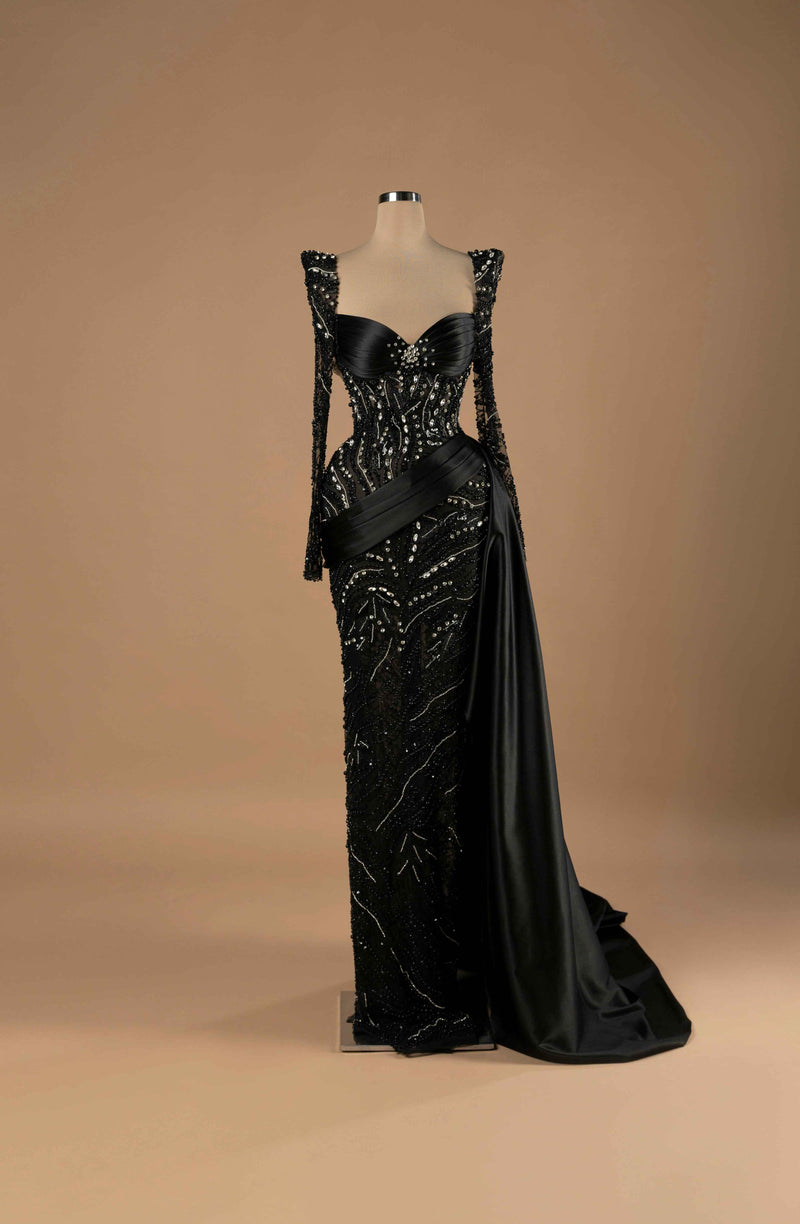 Sihëna Celestial Noir Elegance — black sweetheart long-sleeve column gown with draped satin bust, crystal-beaded illusion body and satin sash and overskirt train.