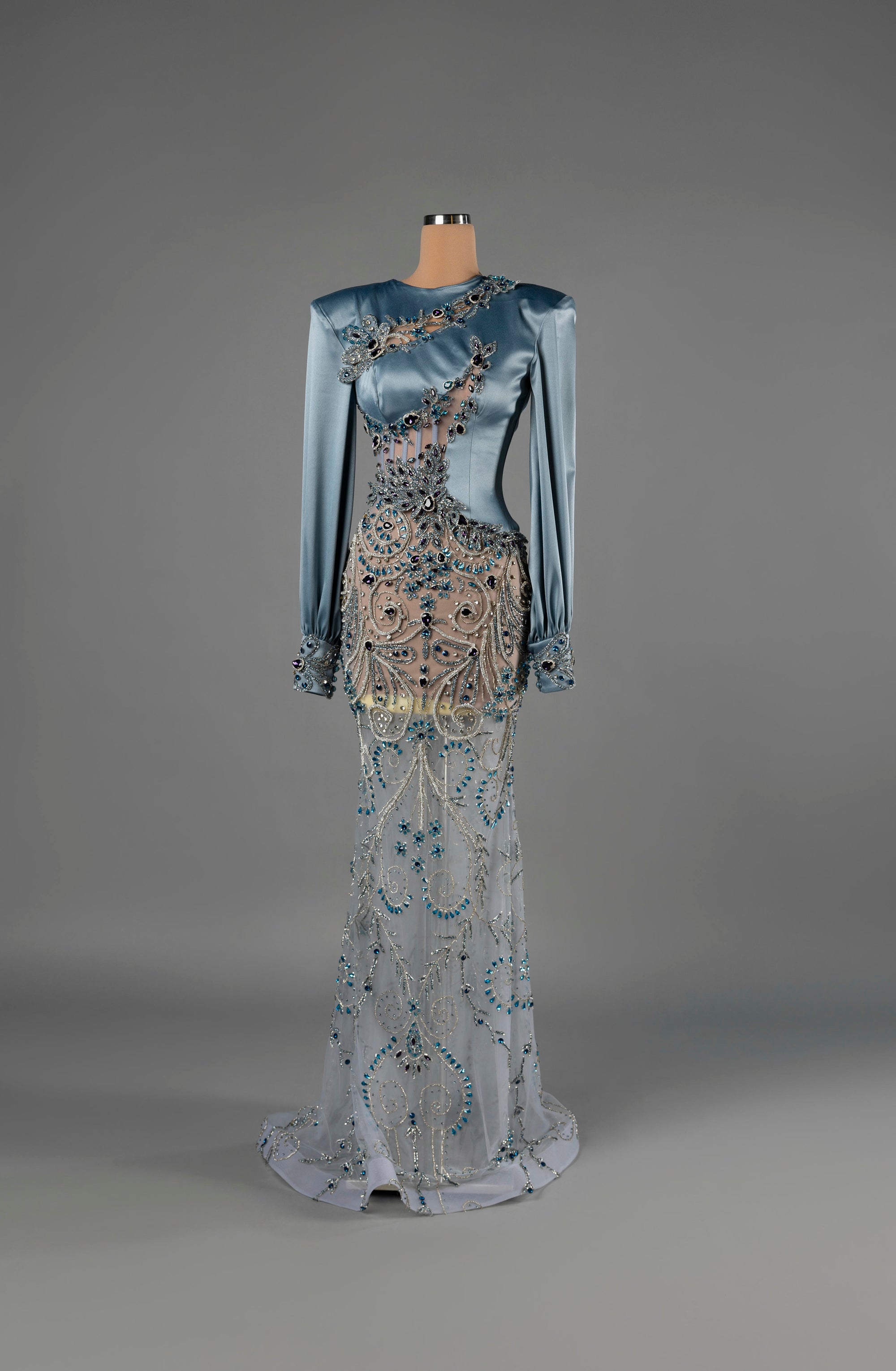 Sihëna Sapphire Enigma — powder-blue high-neck long-sleeve satin mermaid gown with sheer panels and blue crystal beadwork.