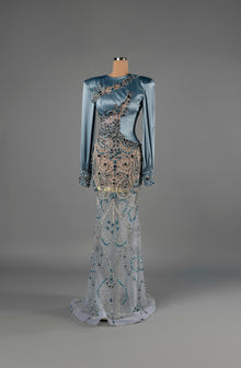 Sihëna Sapphire Enigma — powder-blue high-neck long-sleeve satin mermaid gown with sheer panels and blue crystal beadwork.