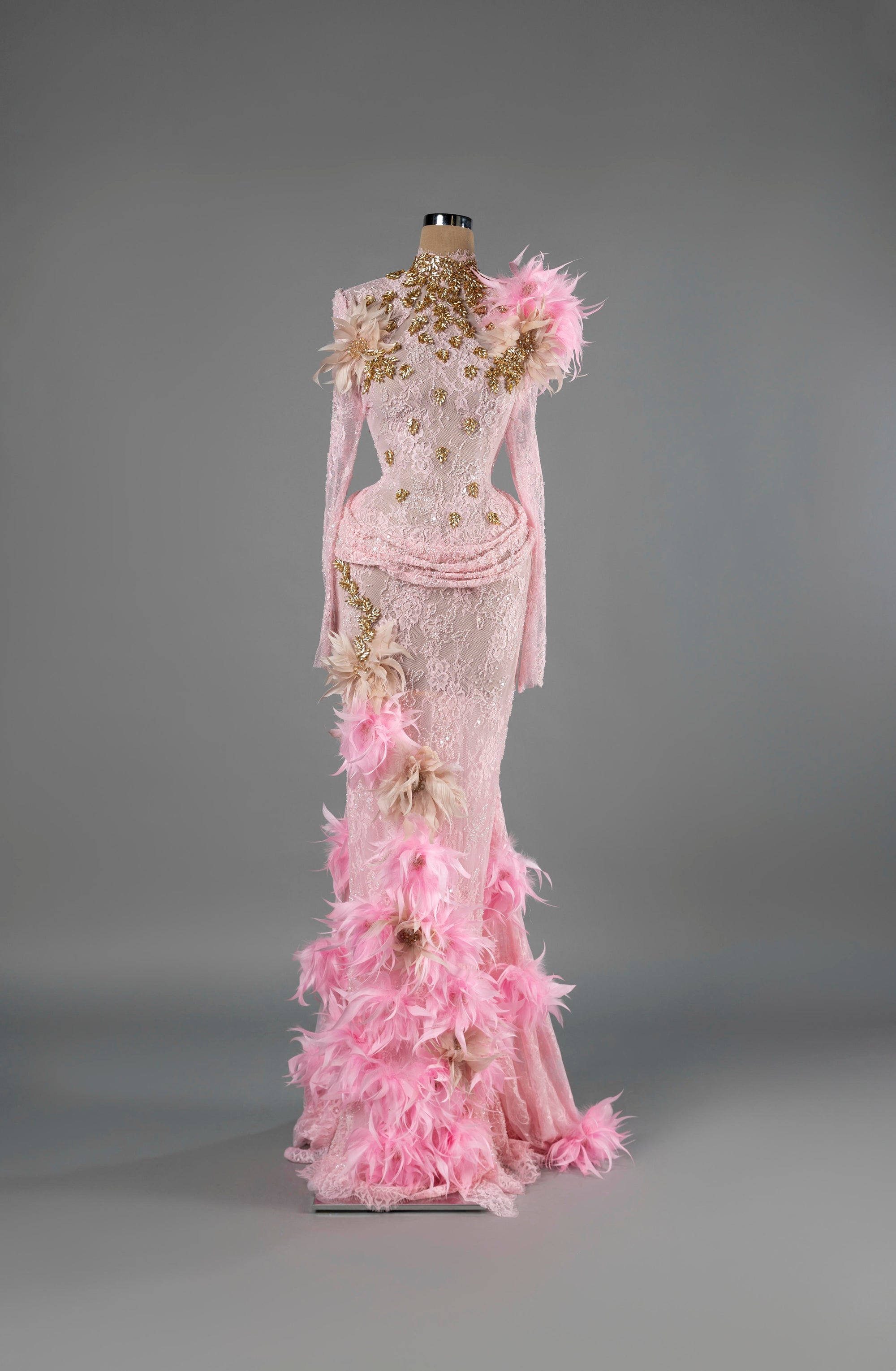 Sihëna Rose Plume — pink high-neck long-sleeve lace mermaid gown with gold leaf beadwork and pink feather floral trim.