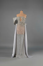 Sihëna Ivory Regalia — silver strapless mermaid gown densely crystal-beaded over sheer nude with structured off-shoulder sleeves and chiffon cape panels.