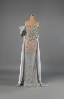 Sihëna Ivory Regalia — silver strapless mermaid gown densely crystal-beaded over sheer nude with structured off-shoulder sleeves and chiffon cape panels.