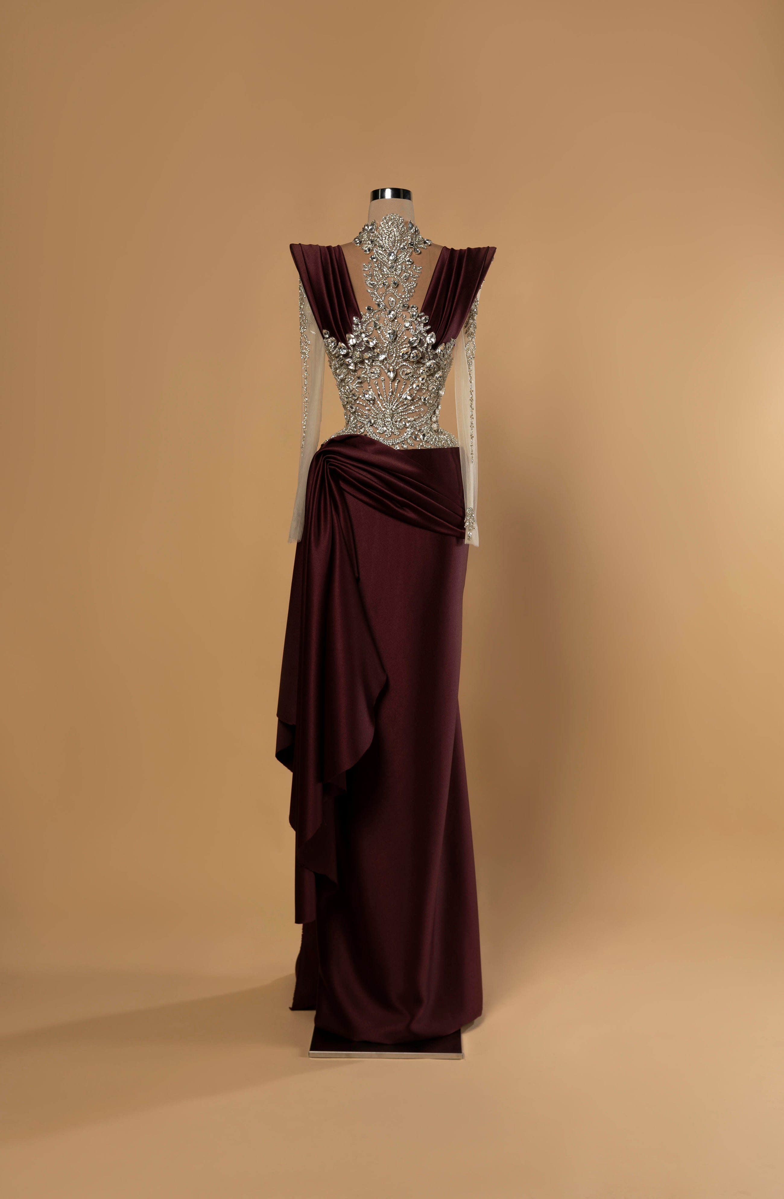 Sihëna Garnet Allure — burgundy high-neck long-sleeve column gown with crystal illusion bodice and draped satin wrap skirt.