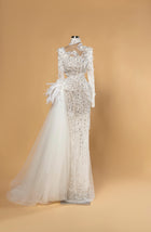 Sihëna Opal Wing Cascade — ivory high-neck long-sleeve mermaid bridal gown in lace with pearl-crystal beadwork, feathers and tulle overskirt.