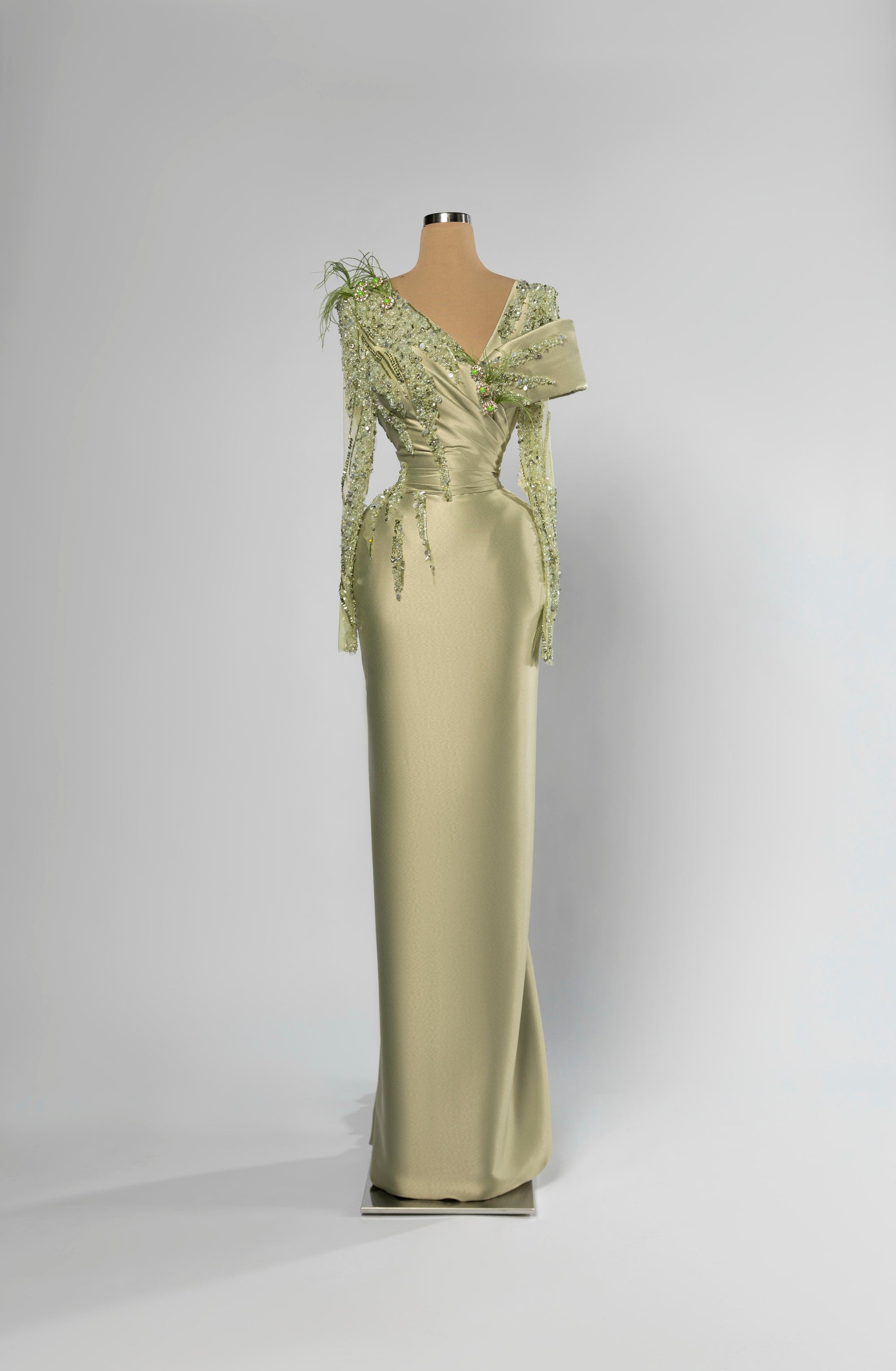 Sihëna Sage Meridian — sage-green asymmetric off-shoulder column evening gown in satin with beaded floral shoulder and feather accent.