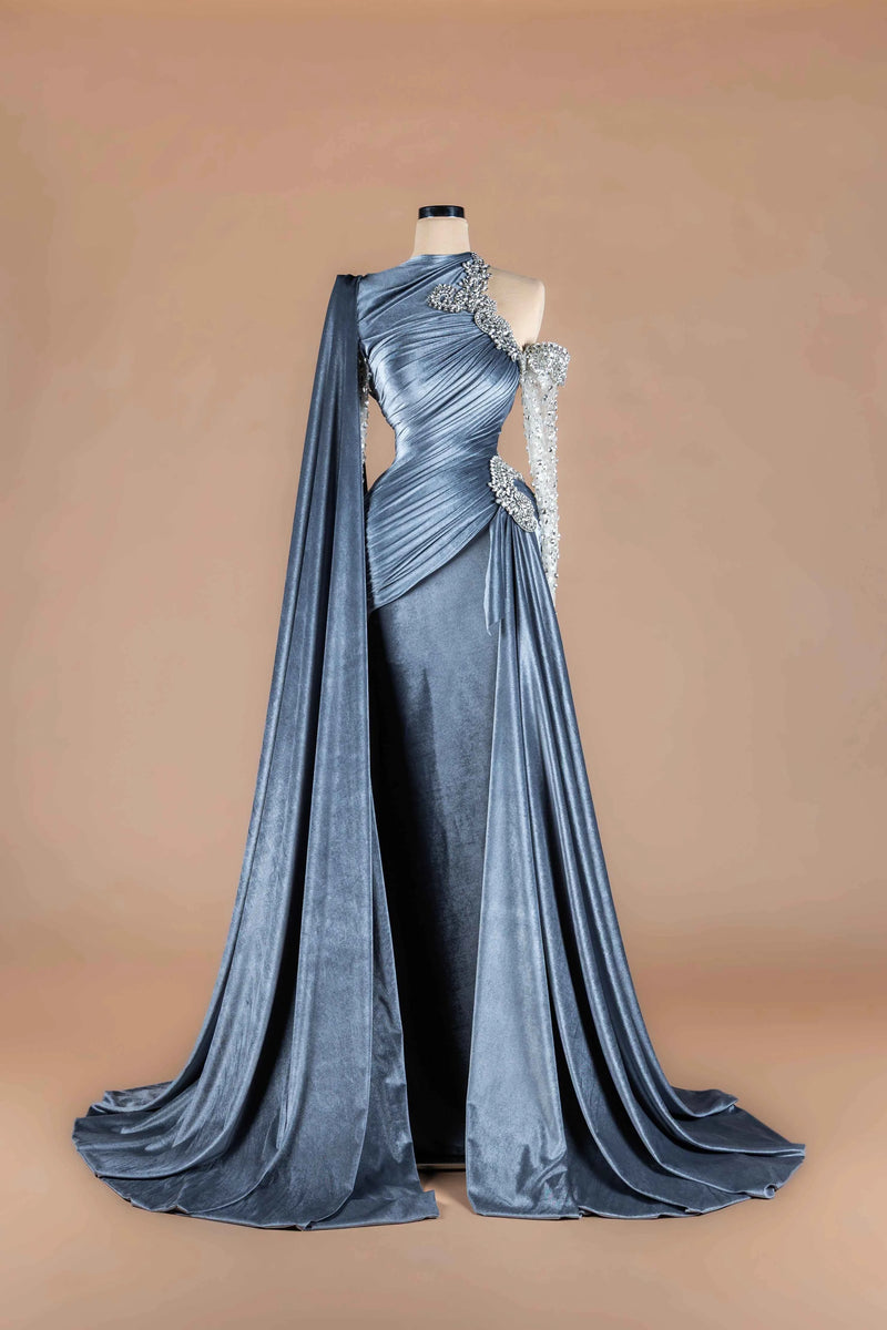 Sihëna Steel Monarch — steel-blue asymmetric one-shoulder velvet gown with crystal appliqué, a beaded sleeve and draped cape.