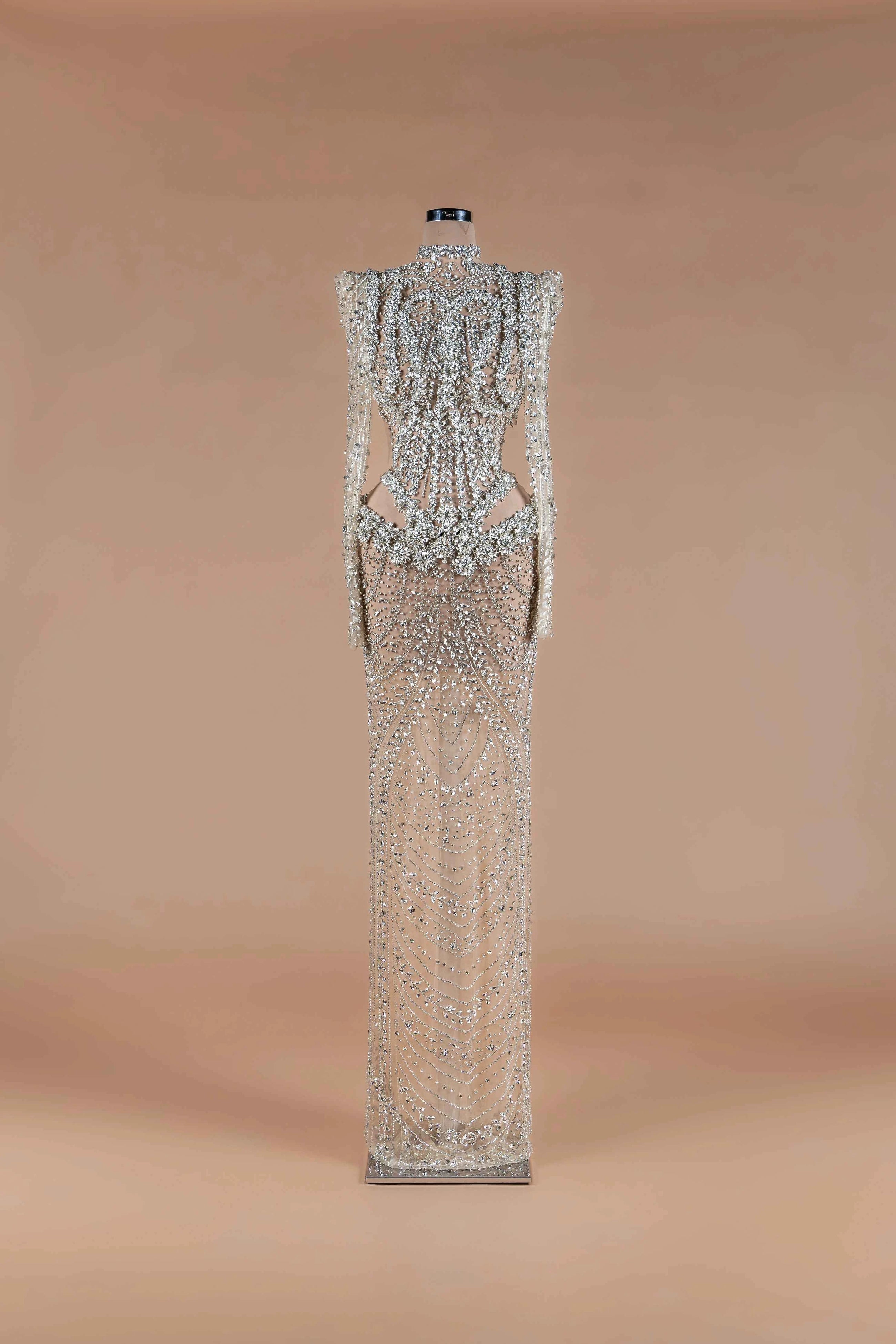 Sihëna Prismatic Cascade — silver high-neck long-sleeve column gown encrusted with crystal and beadwork on sheer nude tulle.