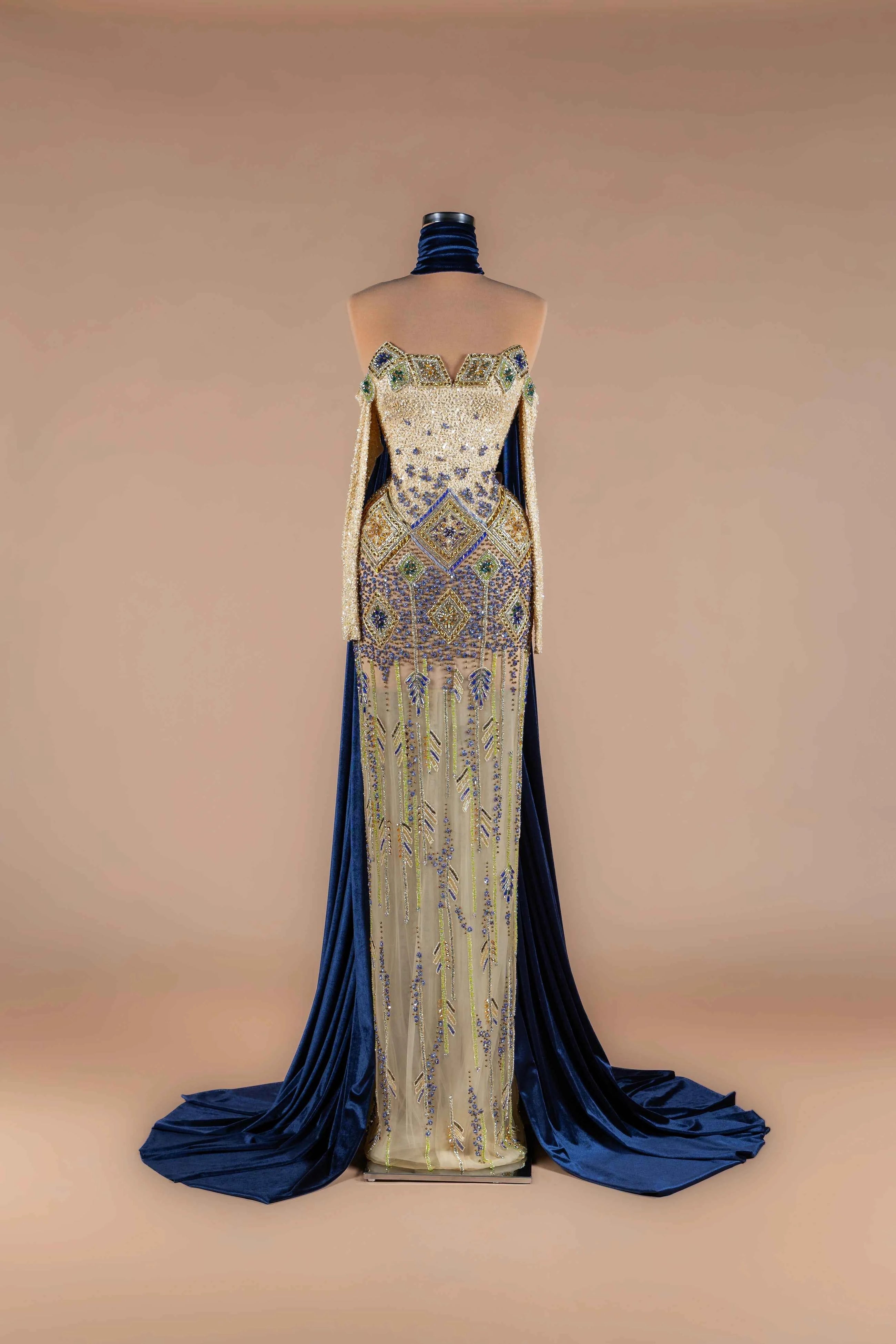 Sihëna Indigo Mosaic — navy strapless off-shoulder mermaid gown with gold-and-blue mosaic beadwork and navy velvet cape train.