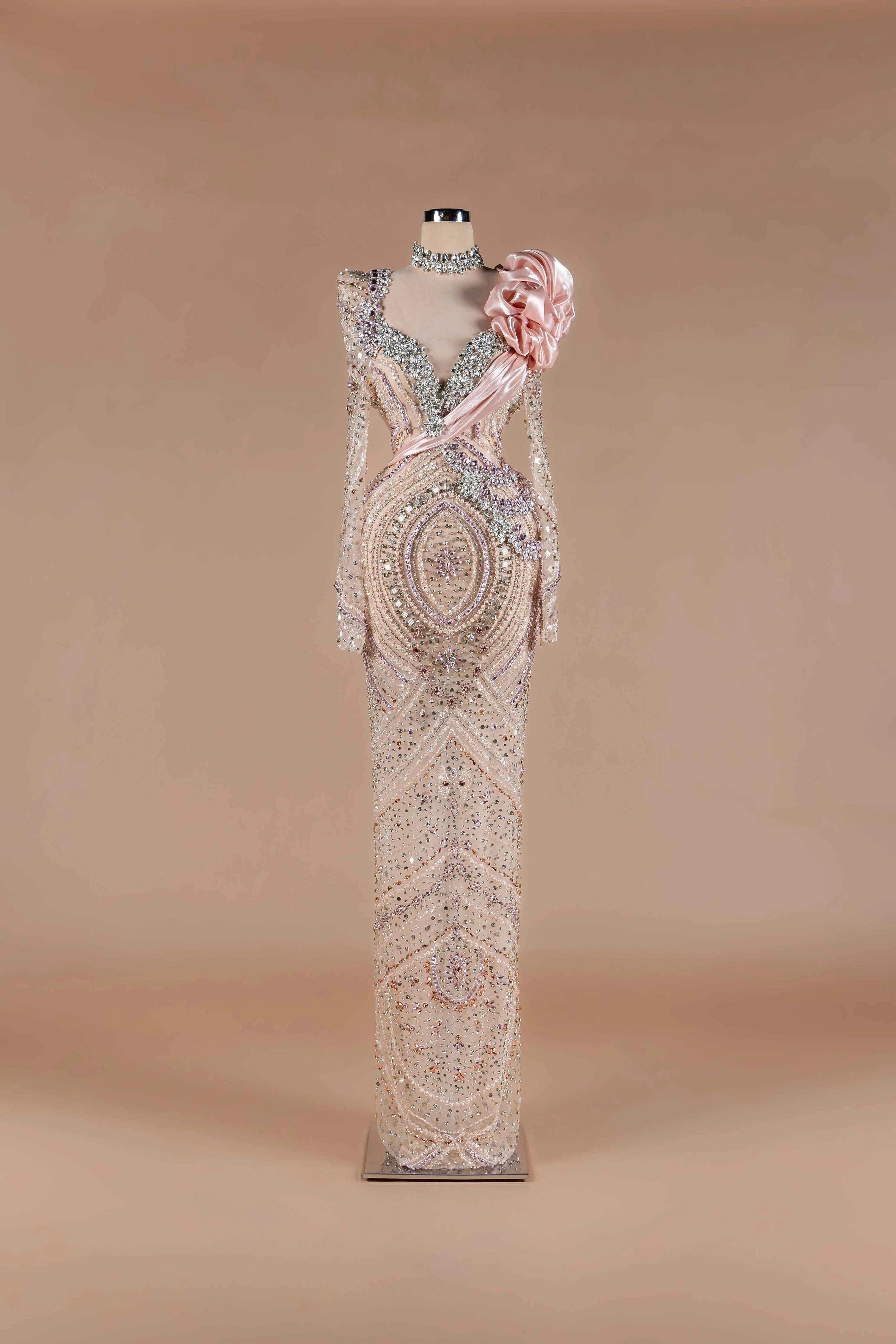 Sihëna Blush Prism Bloom — blush deep-V long-sleeve crystal-and-pearl beaded gown with satin rosette and draped sash.