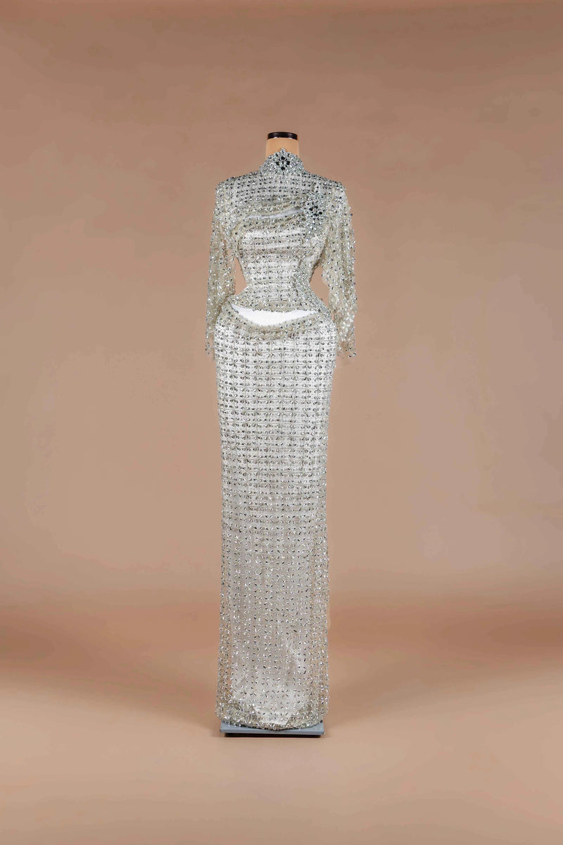 Sihëna Ivory Armor — silver high-neck long-sleeve fully crystal-encrusted column gown with draped sash and waist cutout.