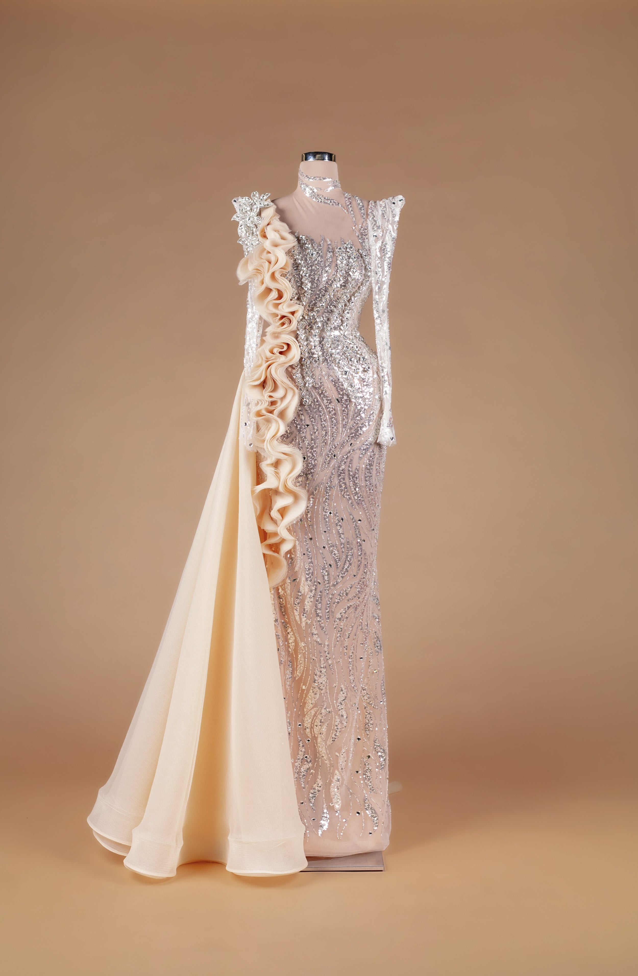 Sihëna Emerald Relic Couture — champagne high-neck long-sleeve crystal-beaded illusion column gown with organza ruffle cascade and overskirt train.