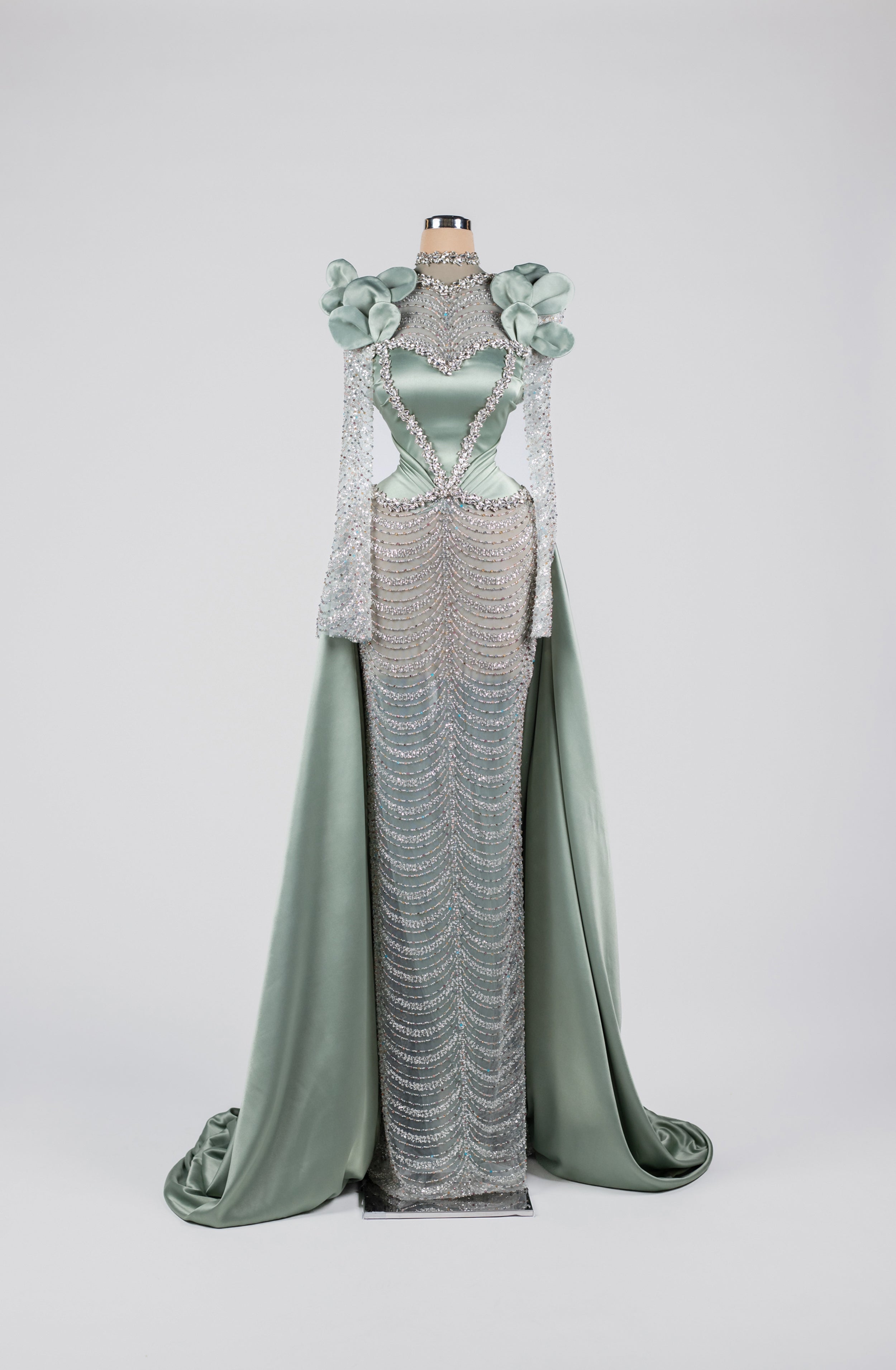 Sihëna Celestine Petal Crest — sage-green high-neck long-sleeve satin gown with floral shoulders, crystal beadwork and chain-drape skirt.